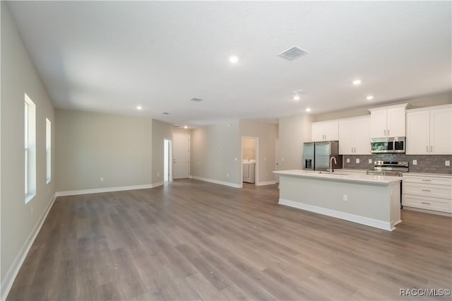 kitchen featuring backsplash, a center island with sink, light wood-type flooring, appliances with stainless steel finishes, and white cabinetry