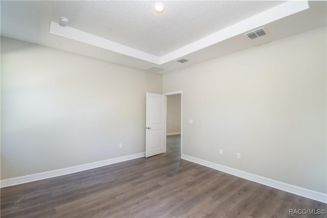 spare room featuring dark hardwood / wood-style floors, a raised ceiling, and a textured ceiling