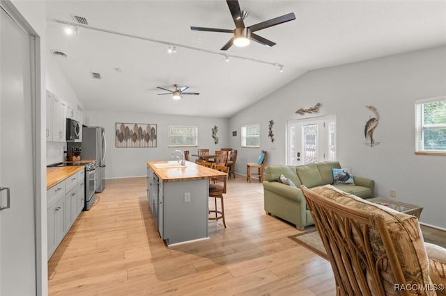 kitchen with wooden counters, stainless steel appliances, an island with sink, sink, and a breakfast bar area