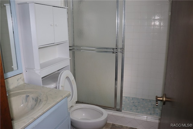 bathroom with tile patterned floors, vanity, a shower with shower door, and toilet