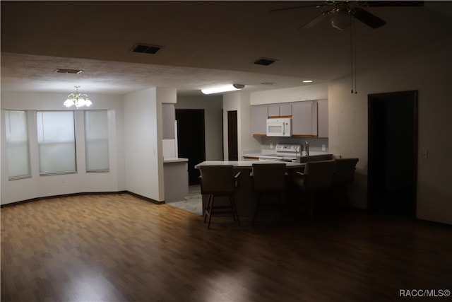 kitchen with gray cabinetry, white appliances, a kitchen breakfast bar, dark hardwood / wood-style flooring, and kitchen peninsula