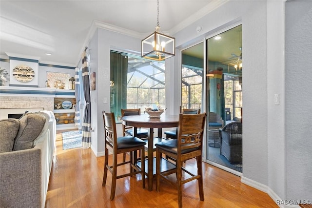 dining area with a stone fireplace, crown molding, wood-type flooring, and an inviting chandelier