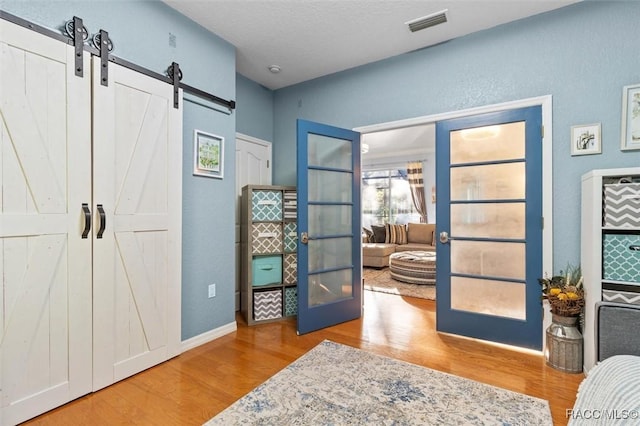 living area with a barn door, wood-type flooring, a textured ceiling, and french doors