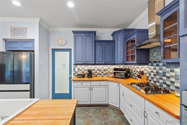 kitchen with wooden counters, stainless steel appliances, white cabinetry, and wall chimney range hood