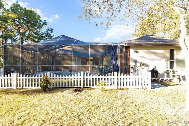 rear view of property featuring a yard and glass enclosure