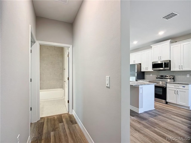 kitchen featuring light stone counters, white cabinets, stainless steel appliances, hardwood / wood-style floors, and backsplash