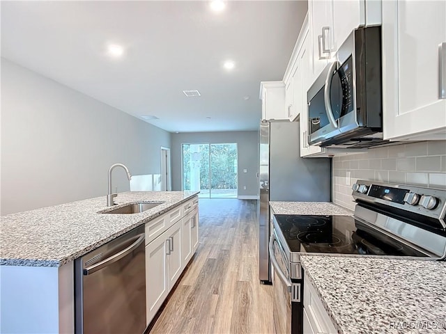 kitchen featuring sink, white cabinets, light hardwood / wood-style floors, stainless steel appliances, and a center island with sink