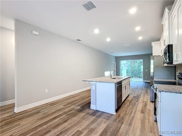 kitchen featuring appliances with stainless steel finishes, sink, white cabinets, light stone counters, and a center island with sink