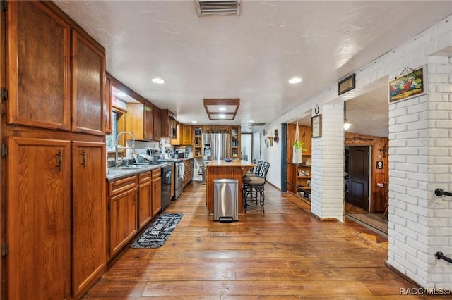 kitchen with sink, appliances with stainless steel finishes, hardwood / wood-style floors, a kitchen bar, and a kitchen island