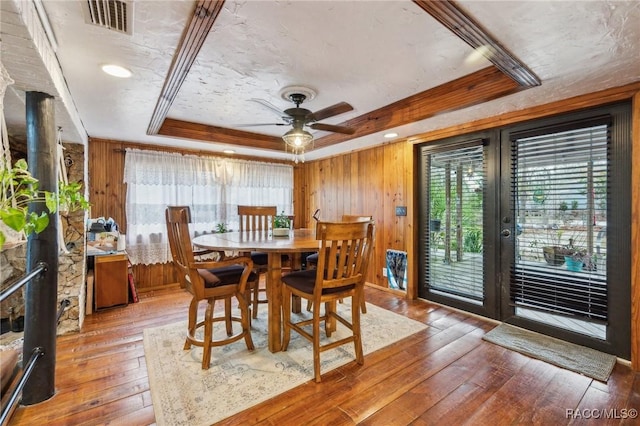 dining room with hardwood / wood-style flooring, ceiling fan, wooden walls, ornamental molding, and a raised ceiling