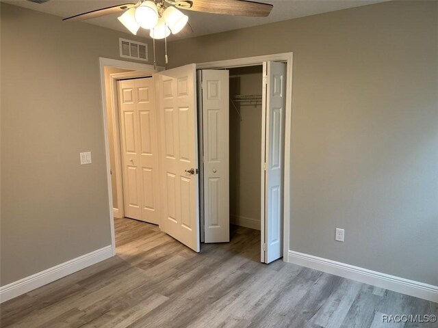 unfurnished bedroom featuring visible vents, a closet, baseboards, and wood finished floors