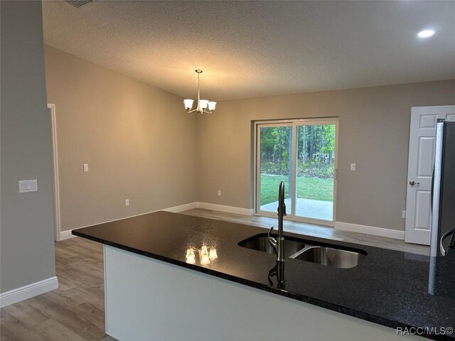 unfurnished dining area with light wood-type flooring, a textured ceiling, baseboards, and an inviting chandelier