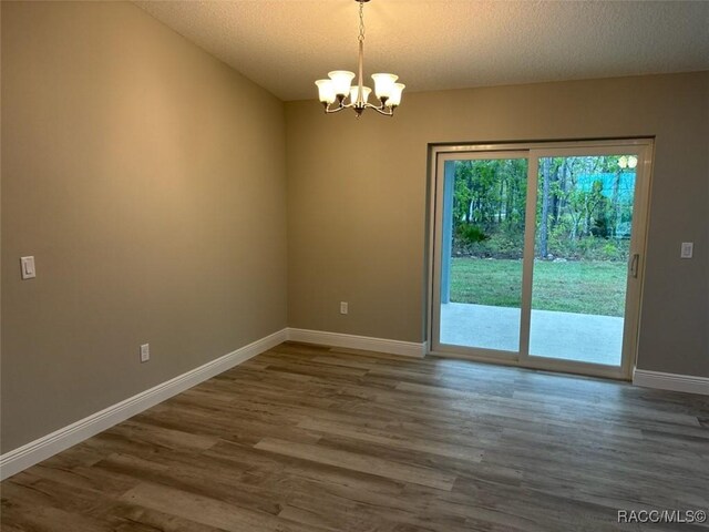 empty room with baseboards, visible vents, wood finished floors, a textured ceiling, and a chandelier