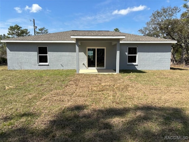 rear view of house with roof with shingles, a yard, and stucco siding