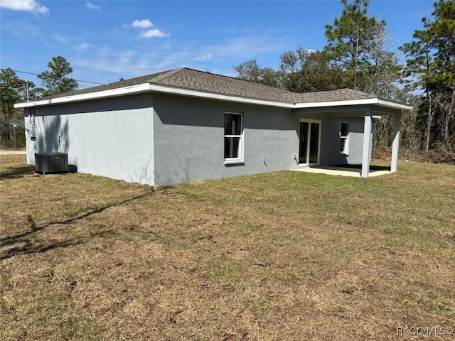 rear view of house with a shingled roof, a patio area, a lawn, and stucco siding