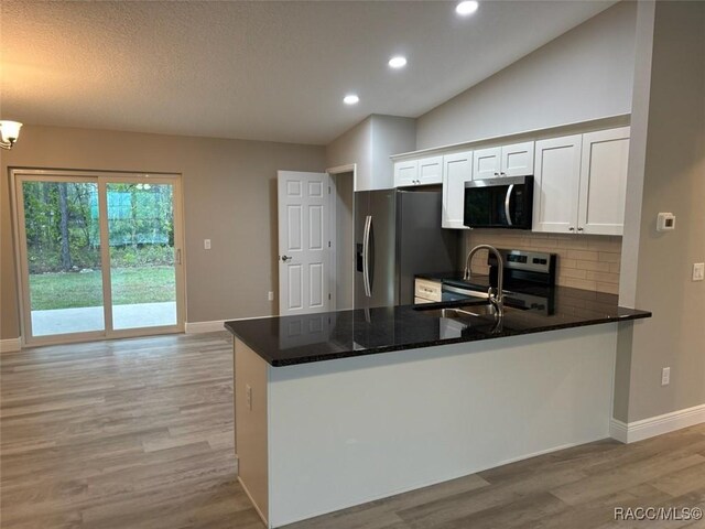 kitchen featuring appliances with stainless steel finishes, white cabinets, a sink, wood finished floors, and a peninsula