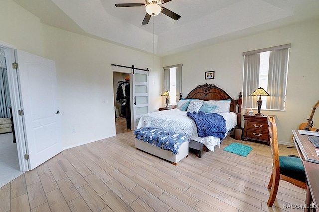 bedroom featuring a barn door, baseboards, a raised ceiling, light wood-style flooring, and a walk in closet