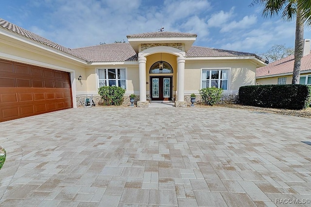 property entrance with an attached garage, a tile roof, french doors, decorative driveway, and stucco siding