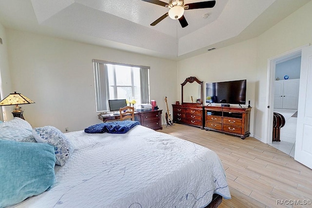 bedroom with ceiling fan, light wood-type flooring, a raised ceiling, and visible vents