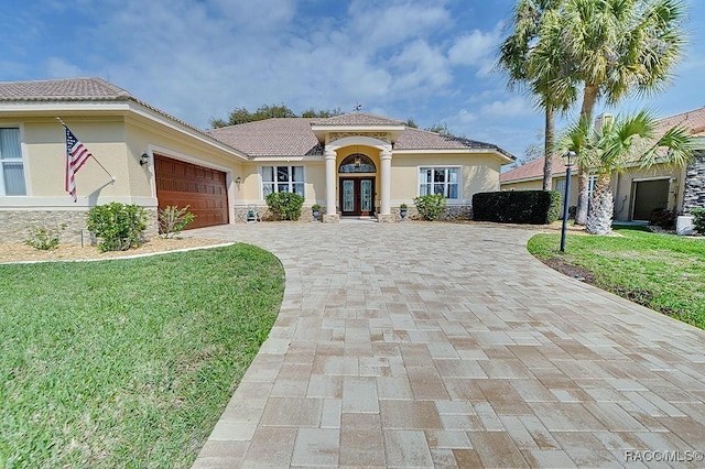 mediterranean / spanish home with a garage, french doors, decorative driveway, stucco siding, and a front yard