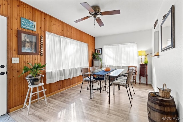 dining space with light hardwood / wood-style flooring, ceiling fan, and wooden walls