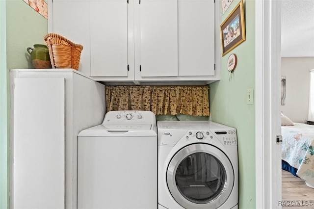 laundry area with cabinets, washing machine and dryer, a textured ceiling, and light hardwood / wood-style flooring