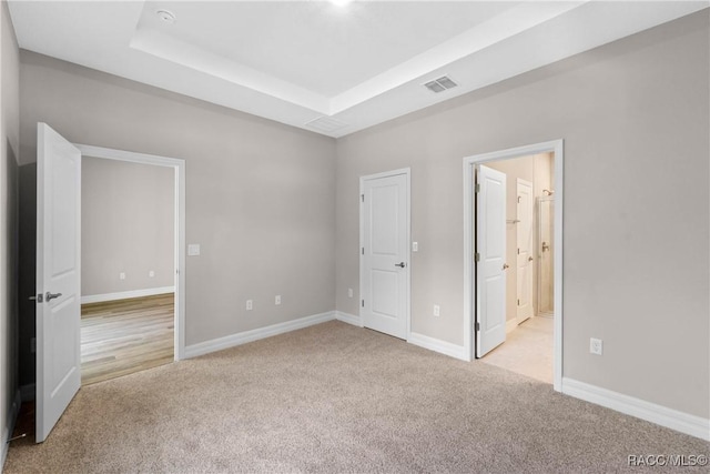 unfurnished bedroom with a raised ceiling, visible vents, carpet flooring, connected bathroom, and baseboards