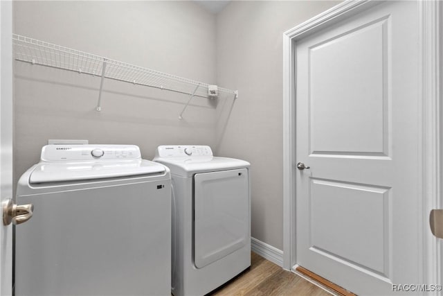 clothes washing area with laundry area, washer and clothes dryer, baseboards, and wood finished floors