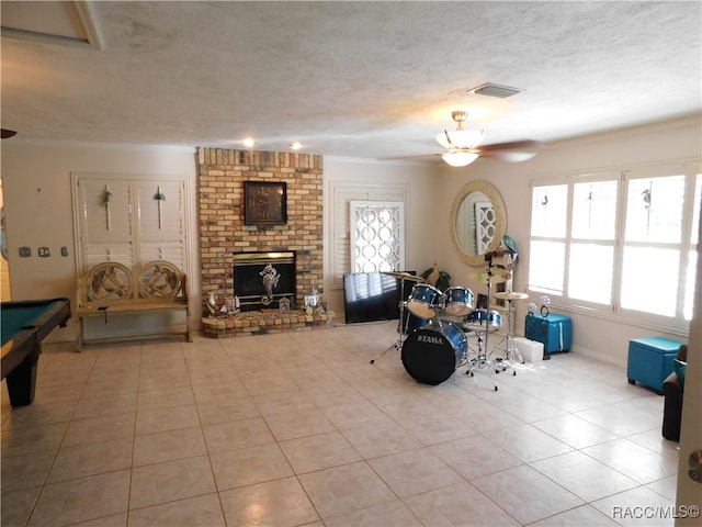 rec room featuring ceiling fan, a healthy amount of sunlight, a textured ceiling, and a brick fireplace