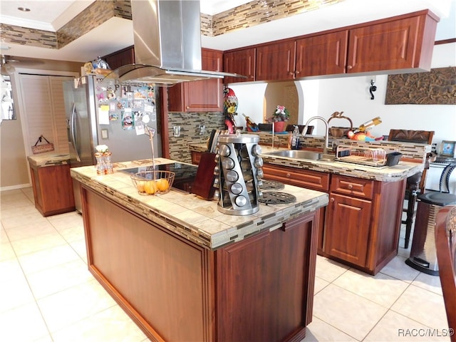 kitchen with ornamental molding, island range hood, sink, light tile patterned floors, and stainless steel refrigerator