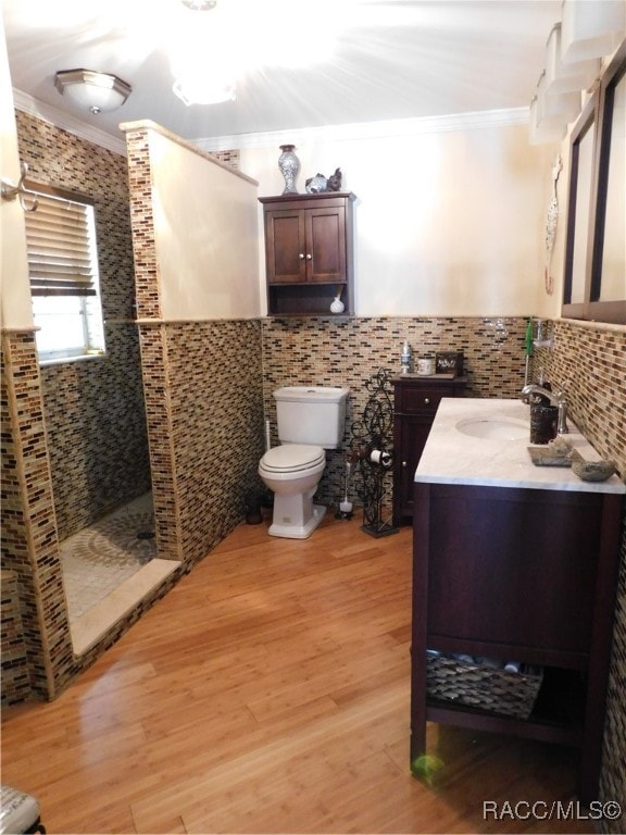 bathroom featuring walk in shower, crown molding, wood-type flooring, vanity, and tile walls