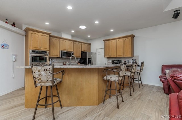 kitchen featuring a kitchen breakfast bar, backsplash, stainless steel appliances, and light hardwood / wood-style floors