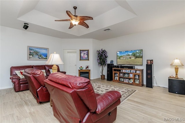 living room featuring a raised ceiling, ceiling fan, and light hardwood / wood-style floors