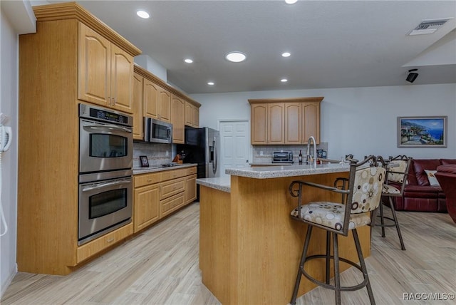 kitchen with light wood-type flooring, tasteful backsplash, a breakfast bar, stainless steel appliances, and a kitchen island with sink