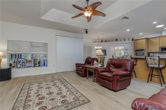 living room featuring a tray ceiling, light hardwood / wood-style flooring, and ceiling fan with notable chandelier