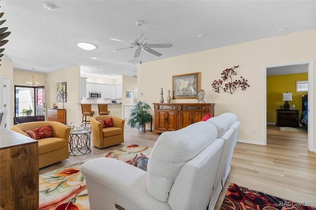 living room featuring ceiling fan with notable chandelier and light hardwood / wood-style flooring