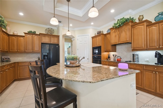 kitchen featuring sink, crown molding, decorative light fixtures, a center island with sink, and black appliances