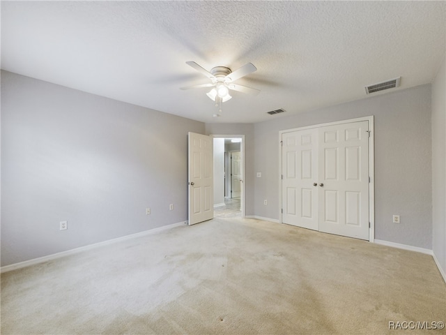 unfurnished bedroom featuring light colored carpet, a textured ceiling, ceiling fan, and a closet