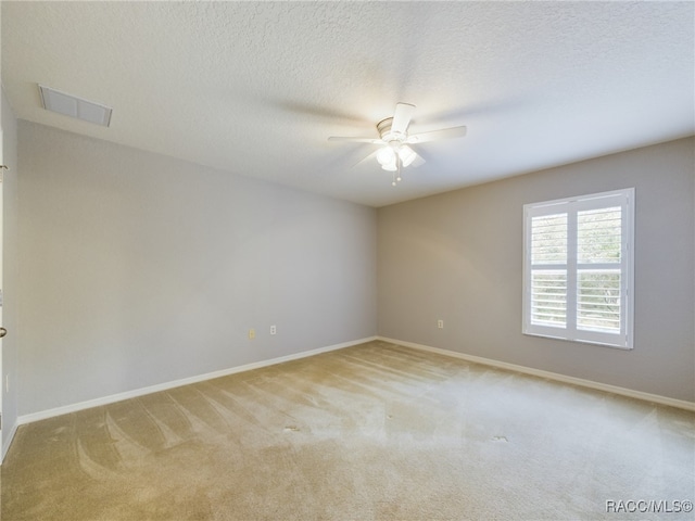 empty room with a textured ceiling, light colored carpet, and ceiling fan