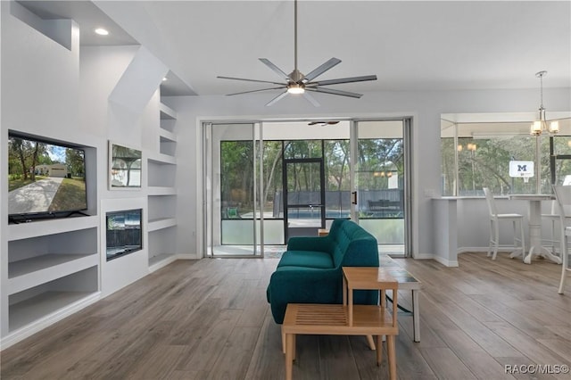 living area with ceiling fan with notable chandelier, built in features, and hardwood / wood-style floors