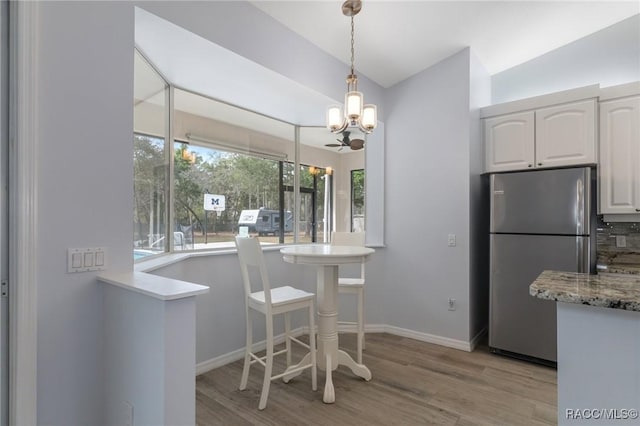 kitchen with lofted ceiling, light hardwood / wood-style floors, stainless steel fridge, white cabinets, and hanging light fixtures