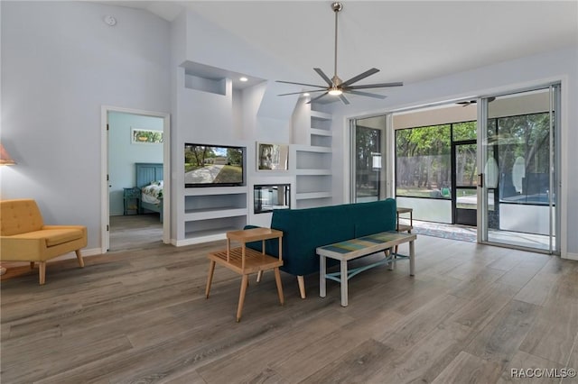 living room with high vaulted ceiling, hardwood / wood-style flooring, ceiling fan, and built in shelves