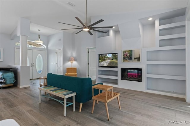 living room featuring ceiling fan, light wood-type flooring, a towering ceiling, and built in features