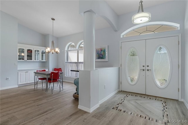 foyer entrance featuring an inviting chandelier, vaulted ceiling, decorative columns, light wood-type flooring, and french doors