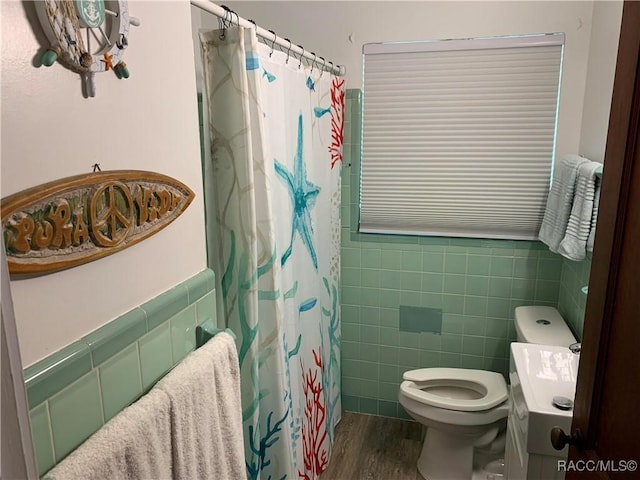 bathroom featuring wainscoting, toilet, a shower with shower curtain, wood finished floors, and tile walls