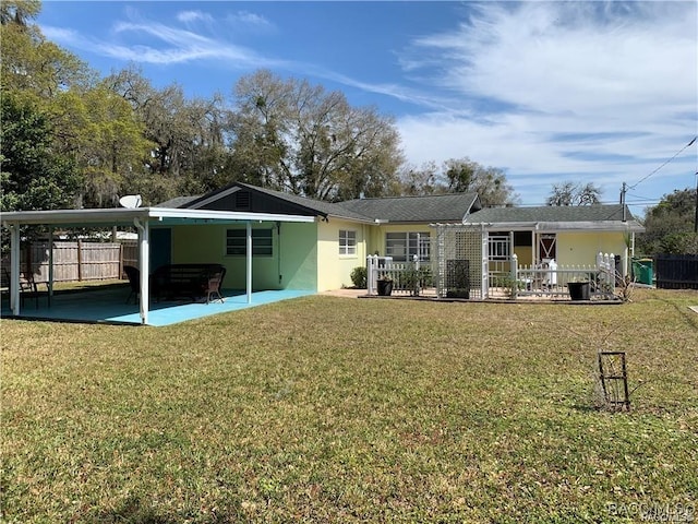 rear view of house with an attached carport, stucco siding, fence, and a lawn