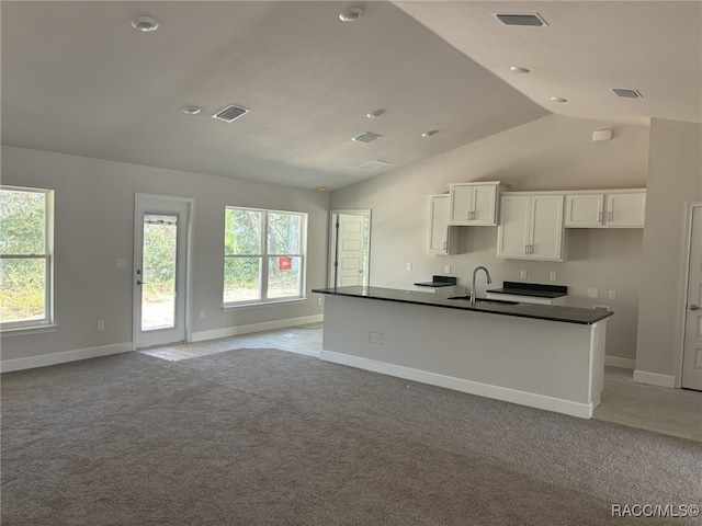 kitchen with light carpet, a kitchen island with sink, sink, white cabinetry, and lofted ceiling