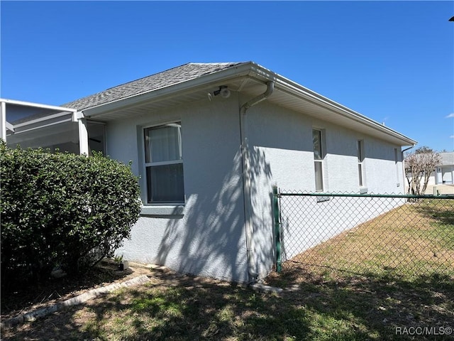 view of property exterior with a yard, fence, a shingled roof, and stucco siding