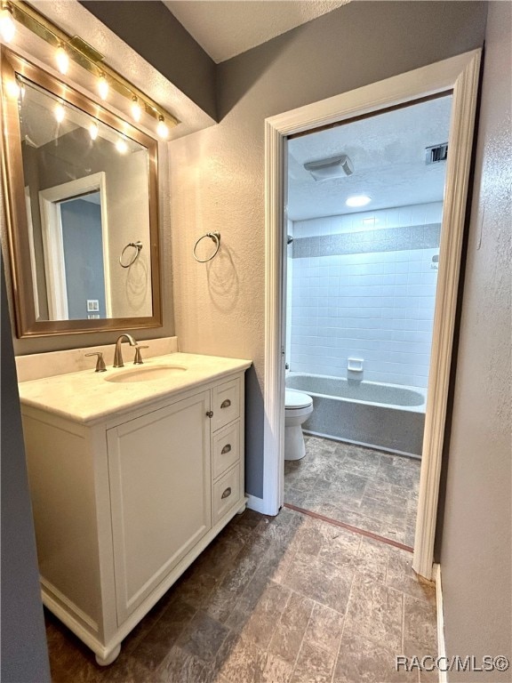 full bathroom featuring tiled shower / bath, vanity, and toilet