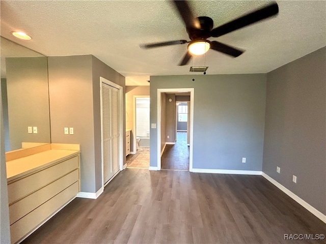 unfurnished bedroom featuring ensuite bath, ceiling fan, a textured ceiling, a closet, and hardwood / wood-style flooring